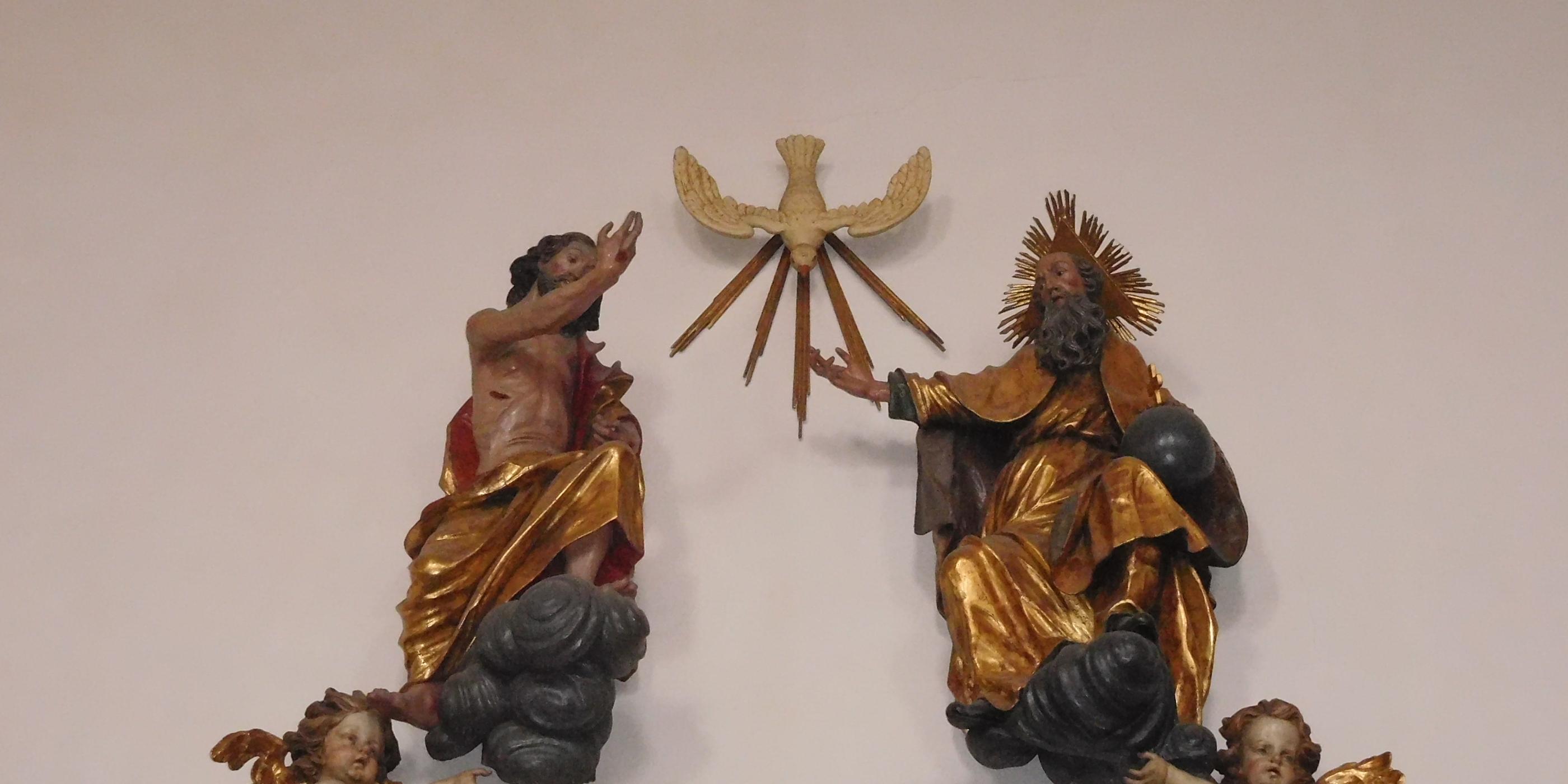 Man sieht als Figuren an einer Wand Jesus, den Heiligen Geist und Gott Vater.
