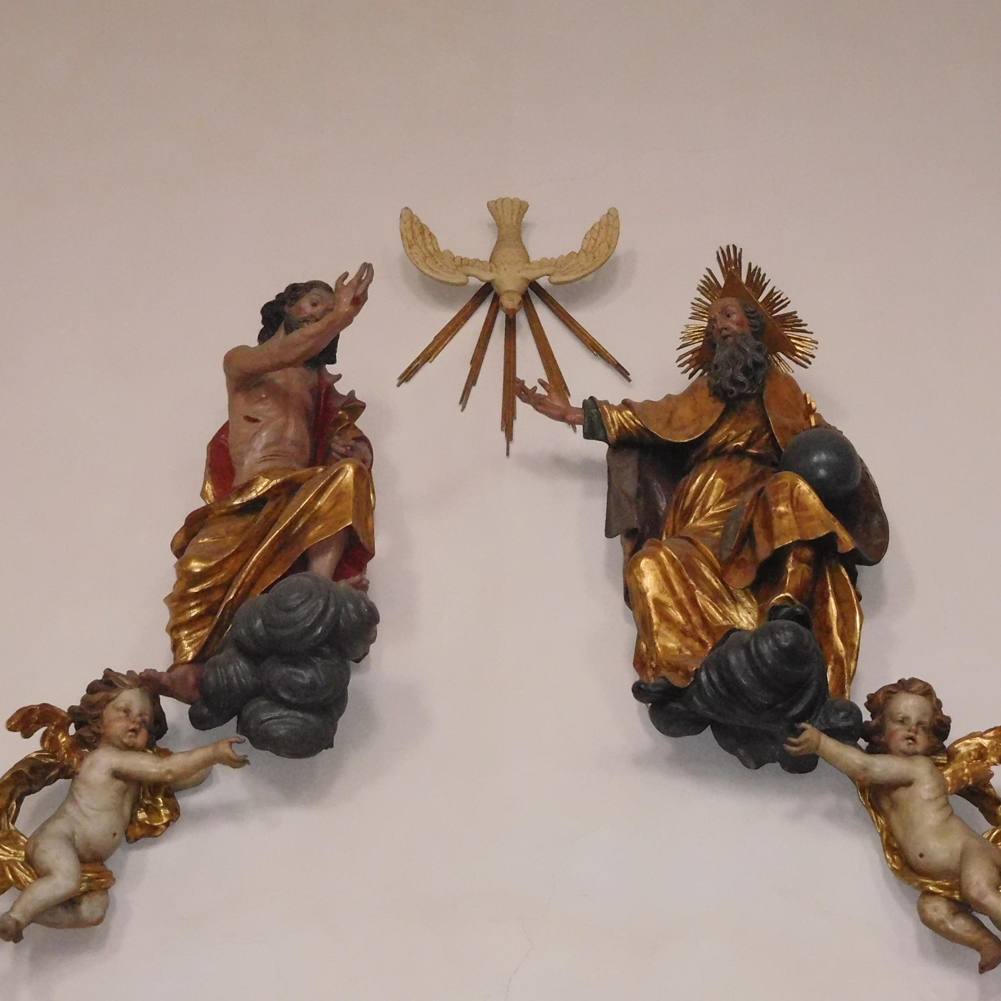 Man sieht als Figuren an einer Wand Jesus, den Heiligen Geist und Gott Vater.
