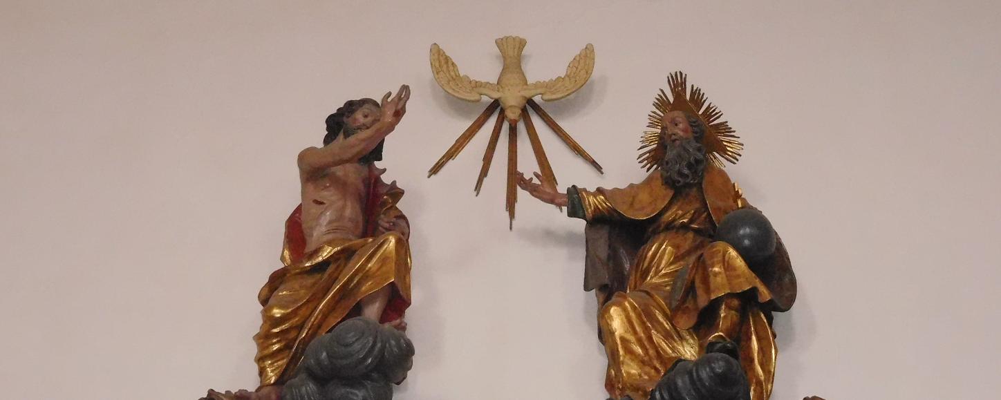Man sieht als Figuren an einer Wand Jesus, den Heiligen Geist und Gott Vater.