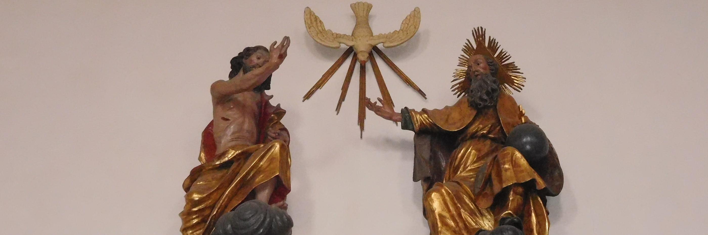 Man sieht als Figuren an einer Wand Jesus, den Heiligen Geist und Gott Vater.