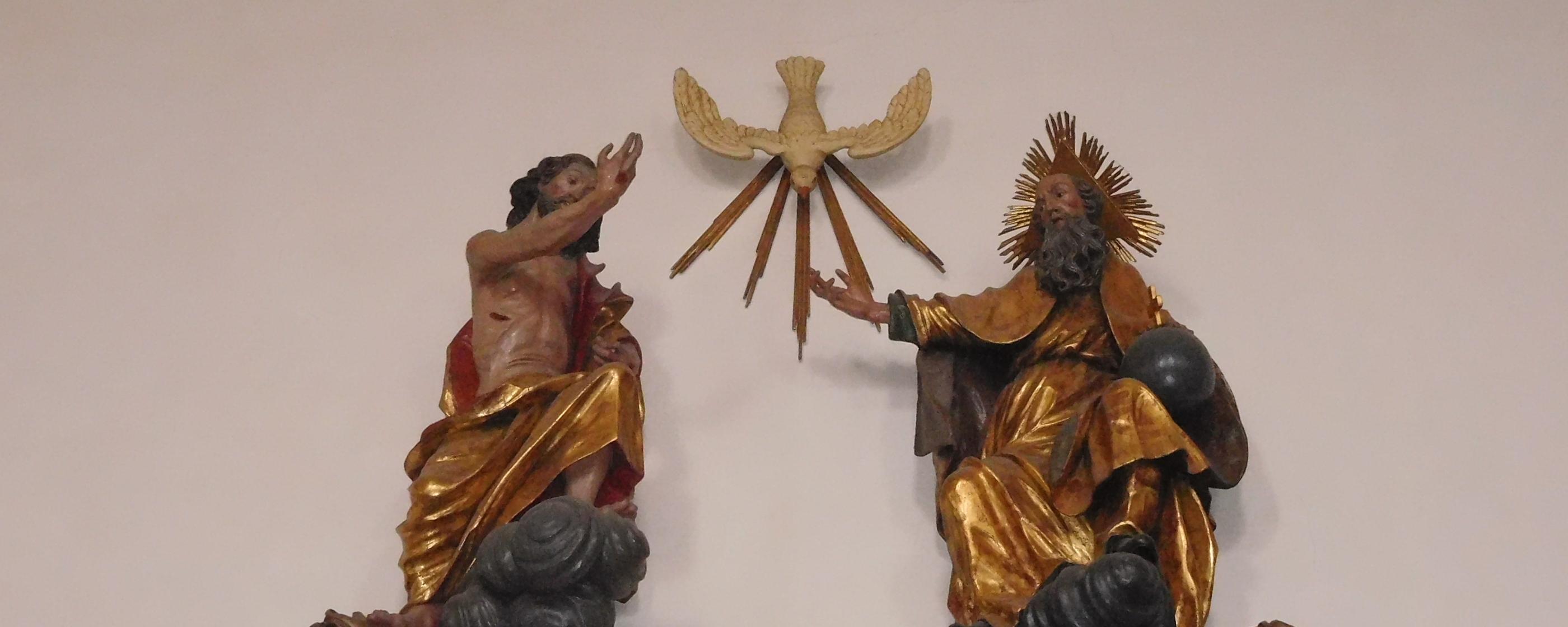 Man sieht als Figuren an einer Wand Jesus, den Heiligen Geist und Gott Vater.