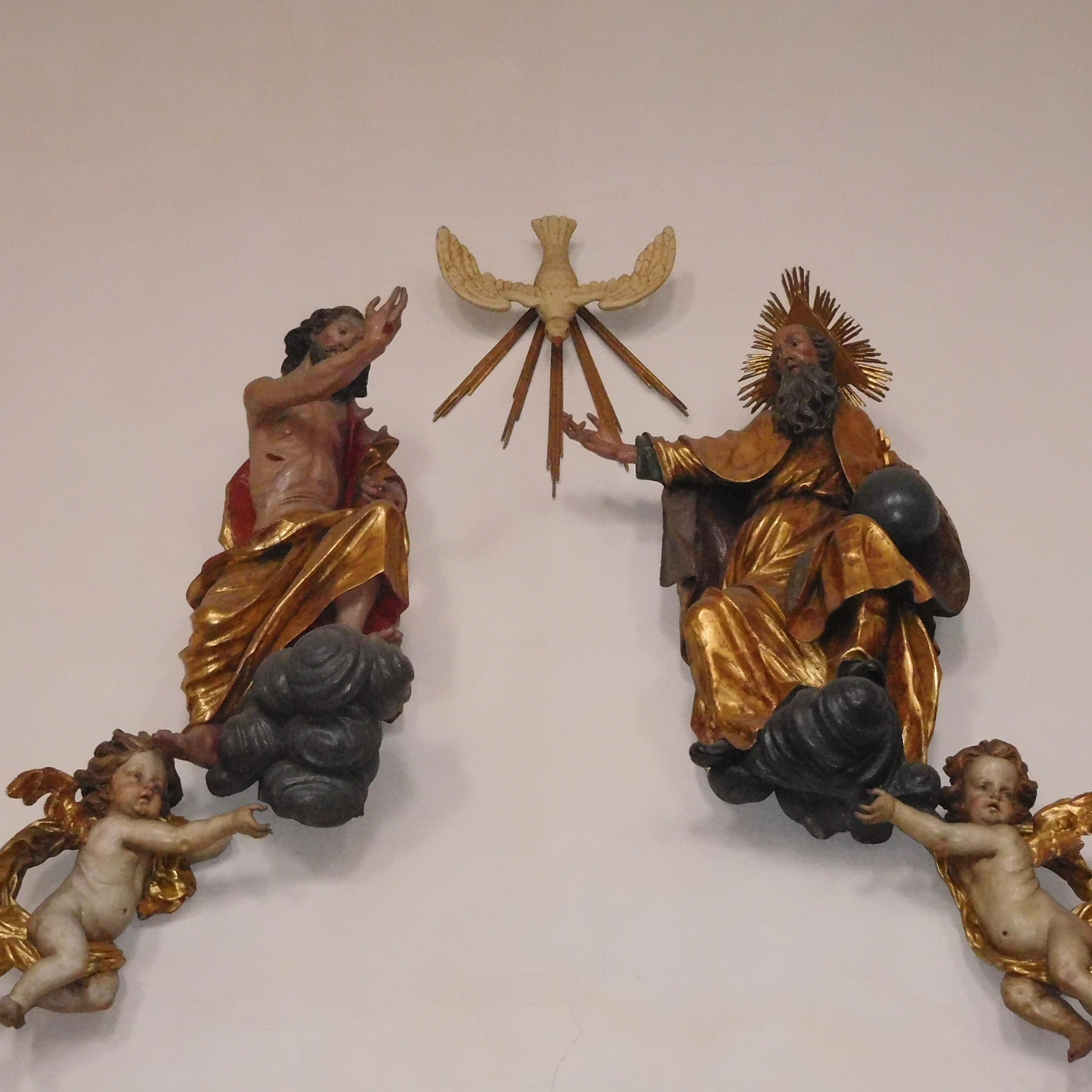 Man sieht als Figuren an einer Wand Jesus, den Heiligen Geist und Gott Vater.