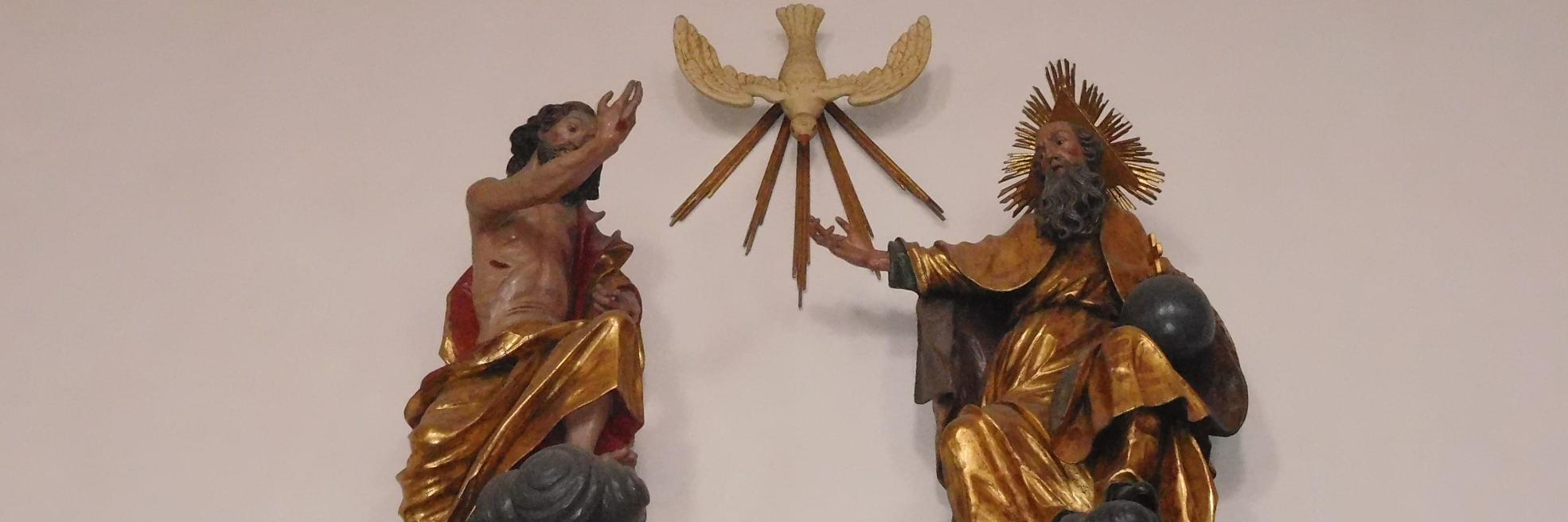 Man sieht als Figuren an einer Wand Jesus, den Heiligen Geist und Gott Vater.