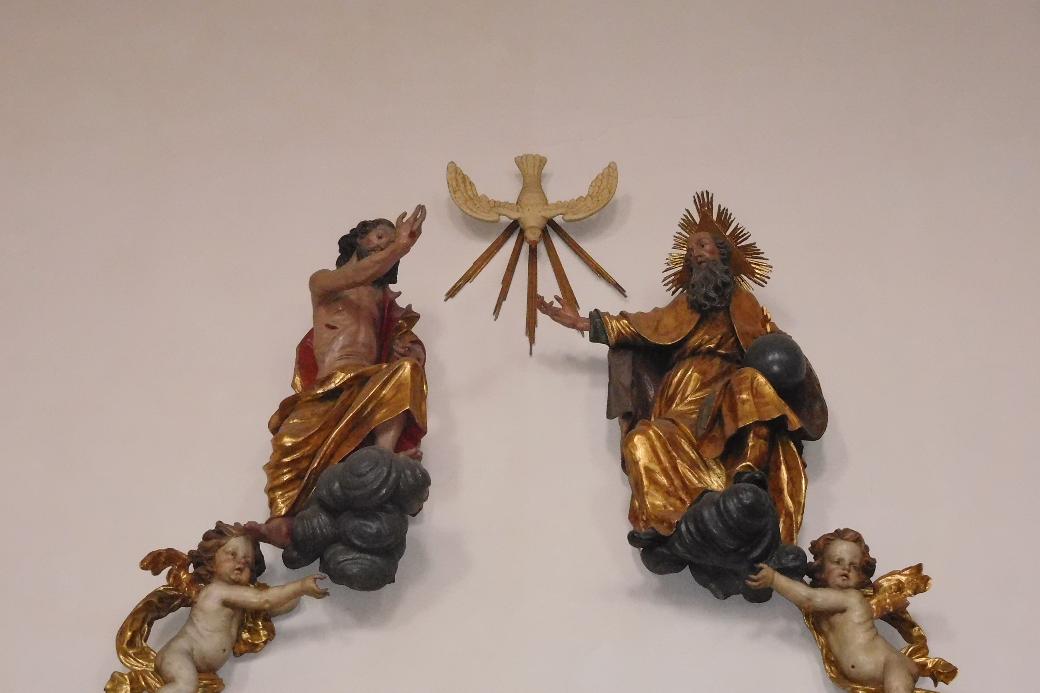 Man sieht als Figuren an einer Wand Jesus, den Heiligen Geist und Gott Vater.
